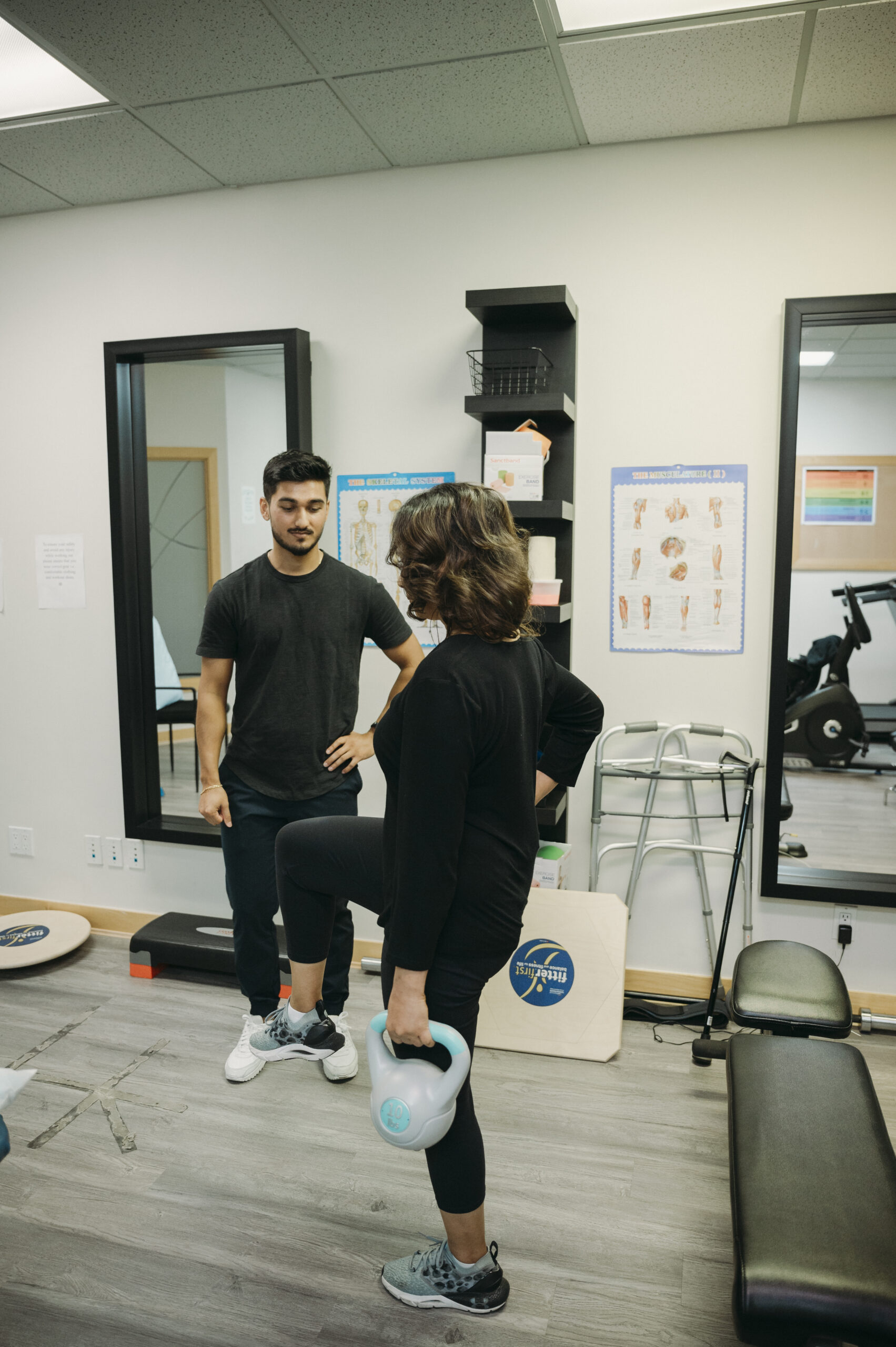 Physiotherapist talking to female patient, who is holding a kettlebell and lifting one leg.